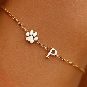Op de afbeelding: Een delicate goudkleurige armband met een pootafdrukbedel en de letter "P". De armband is gemaakt van een fijne ketting en is ontworpen om om de pols te worden gedragen. De pootafdrukbedel is een symbool van dierenliefde.