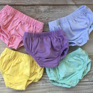 May include: Five pairs of baby bloomers in pastel colors: pink, yellow, purple, light blue, and mint green. The bloomers have elastic waistbands and leg openings, and are made of soft fabric.
