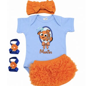 Pu&ograve; includere: Un set di abbigliamento per neonati con un body azzurro chiaro con una grafica di pesce dei cartoni animati, bloomers arancioni a balze, una fascia per capelli con fiocco arancione abbinata e due fasce per i piedi con fiori blu e arancioni. Il nome "Mariel" &egrave; stampato sul body.
