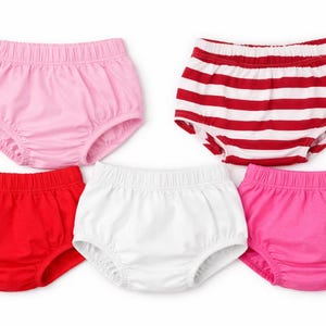 May include: Five pairs of baby bloomers in various colors: pink, red, white, and two shades of pink. One pair features red and white horizontal stripes. All have elastic waistbands.
