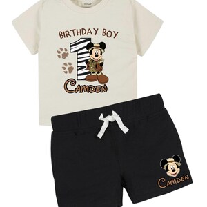 May include: A two-piece baby outfit featuring a cream-colored t-shirt and black shorts. The t-shirt has the text "BIRTHDAY BOY" and "1", with a Mickey Mouse graphic and the name "Camden". The shorts have a Mickey Mouse graphic and the name "Camden".