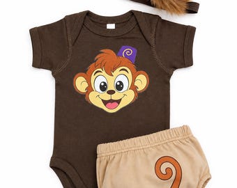 May include: A dark brown short-sleeved bodysuit featuring a cartoon monkey face graphic with a purple fez, paired with tan diaper cover shorts displaying a brown curly tail design, and a matching purple fez hat with brown faux fur trim.