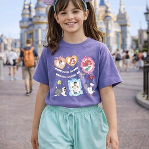 Peut inclure: Une personne porte un t-shirt violet avec des graphiques de personnages Disney et un short bleu clair. Ils portent &eacute;galement un bandeau avec des oreilles de souris et un n&oelig;ud. L'arri&egrave;re-plan montre un ch&acirc;teau et d'autres personnes.