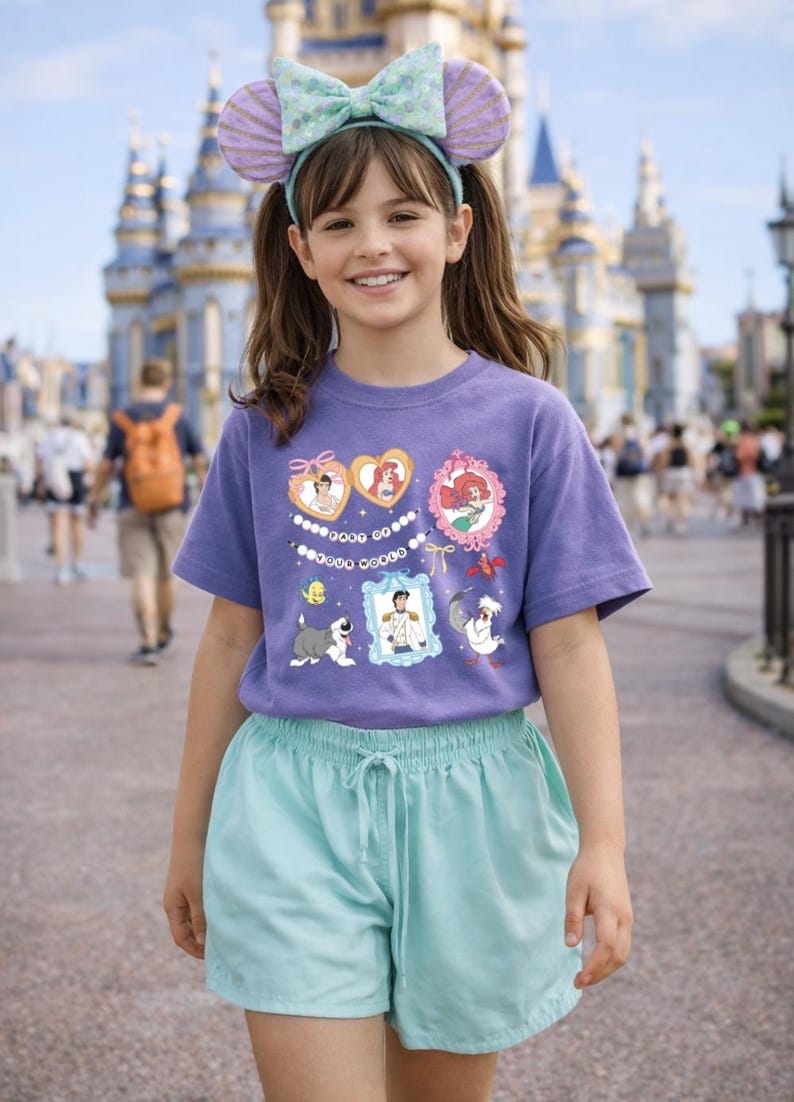 Peut inclure: Une personne porte un t-shirt violet avec des graphiques de personnages Disney et un short bleu clair. Ils portent &eacute;galement un bandeau avec des oreilles de souris et un n&oelig;ud. L'arri&egrave;re-plan montre un ch&acirc;teau et d'autres personnes.