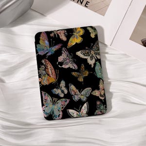 May include: A rectangular electronic reader case featuring a black background decorated with a variety of colorful butterflies in shades of yellow, blue, pink, and orange. The butterflies are depicted in different sizes and wing patterns.