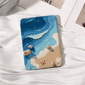 May include: A tablet case featuring a beach scene with blue waves, tan sand, and seashells. The design includes a starfish and various shell shapes, creating a coastal theme. The case has a textured, artistic appearance.