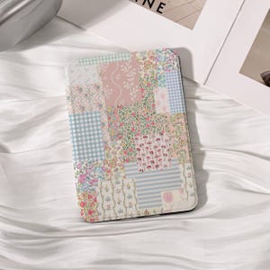Peut inclure: Une housse de liseuse rectangulaire présentant un motif patchwork composé de divers imprimés floraux, vichy et rayés dans des tons pastel doux de rose, bleu, vert et blanc. La couverture affiche un collage de petites fleurs et de lignes.