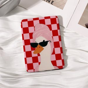 May include: A rectangular case featuring a cartoon goose wearing sunglasses and a pink towel on its head. The case has a red and pink checkered pattern. The goose has an orange beak and is set against a white background.