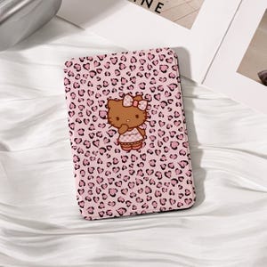 May include: A pink phone case with a leopard print pattern of dark pink hearts and spots. The case features a cartoon image of Hello Kitty with a bow and dress.