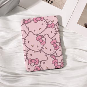Puede incluir: Una funda de teléfono rosa con un patrón repetido del personaje Hello Kitty y lazos rosas. La funda tiene un borde negro y está sobre un fondo blanco. Un accesorio lindo y juguetón.