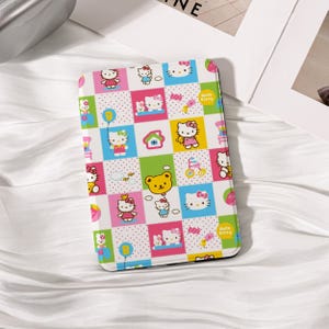 Może przedstawiać: Kolorowe etui na tablet z patchworkowym wzorem. Wzór przedstawia postacie Hello Kitty w różnych pozach, na kwadratach w kolorze różowym, niebieskim, zielonym i żółtym. Na niektórych kwadratach widnieje napis "Hello Kitty".