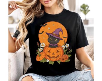 May include: Black t-shirt with a Halloween-themed graphic. A black cat wearing a purple witch's hat is inside a carved pumpkin, set against an orange moon. Bats, flowers, and a small pumpkin complete the design.