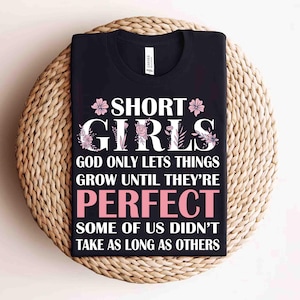 Könnte beinhalten: Schwarzes T-Shirt mit dem weißen Schriftzug "SHORT GIRLS" mit floralen Akzenten. Das Shirt enthält auch das Zitat "GOD ONLY LETS THINGS GROW UNTIL THEY'RE PERFECT. SOME OF US DIDN'T TAKE AS LONG AS OTHERS."