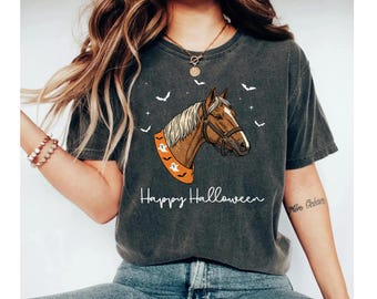 May include: Dark gray t-shirt featuring a brown horse head with a white mane, wearing a Halloween-themed scarf with ghost and pumpkin designs. The words "Happy Halloween" are written below the horse image, with bats and stars.