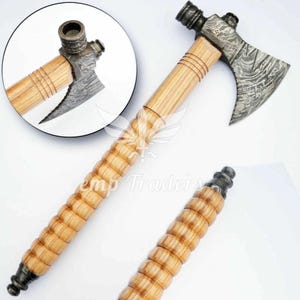 May include: A handcrafted tomahawk with a wooden handle and a patterned steel blade. The handle features a ridged design for grip. The axe head has a pipe bowl. The overall design is rustic and detailed.