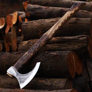 May include: A handcrafted axe with a wooden handle and a silver-colored blade. The handle features a dark wood grain pattern and etched designs. The axe is resting on a pile of dark brown logs, suggesting a rustic or outdoor theme.