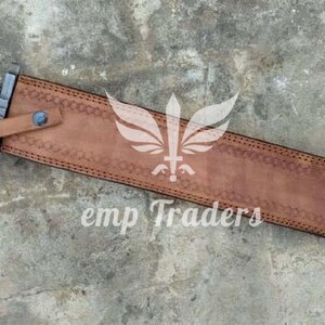 Puede incluir: Una espada romana gladius con una funda de cuero marr&oacute;n. La espada tiene un mango negro y plateado con detalles dorados. La funda est&aacute; grabada con un patr&oacute;n decorativo y el texto "emp Traders".