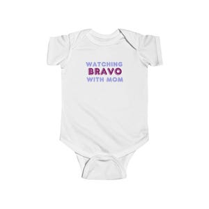 May include: White baby onesie with the text "Watching Bravo with Mom" in purple and pink.