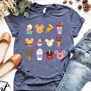 May include: A navy blue t-shirt with a variety of Disney-themed food and drink graphics, including Mickey Mouse ears, ice cream, popcorn, and a donut.