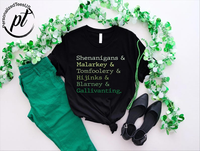 May include: Black t-shirt with the text "Shenanigans & Malarkey & Tomfoolery & Hijinks & Blarney & Gallivanting" in green. The shirt is paired with green pants and black shoes, decorated with green and white garland.