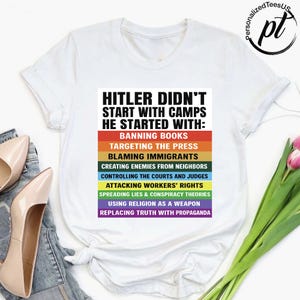 May include: White t-shirt with the text "HITLER DIDN'T START WITH CAMPS HE STARTED WITH:" followed by a list of actions in a rainbow-colored design. The shirt also has the logo "PersonalizedTeesUS".