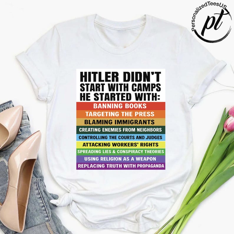 May include: White t-shirt with the text "HITLER DIDN'T START WITH CAMPS HE STARTED WITH:" followed by a list of actions in a rainbow-colored design. The shirt also has the logo "PersonalizedTeesUS".