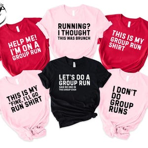 May include: A collection of six short-sleeved t-shirts in red, light pink, and black. Each shirt features bold black or white text related to group running, including phrases like "Help me! I'm on a group run" and "Running? I thought this was brunch."