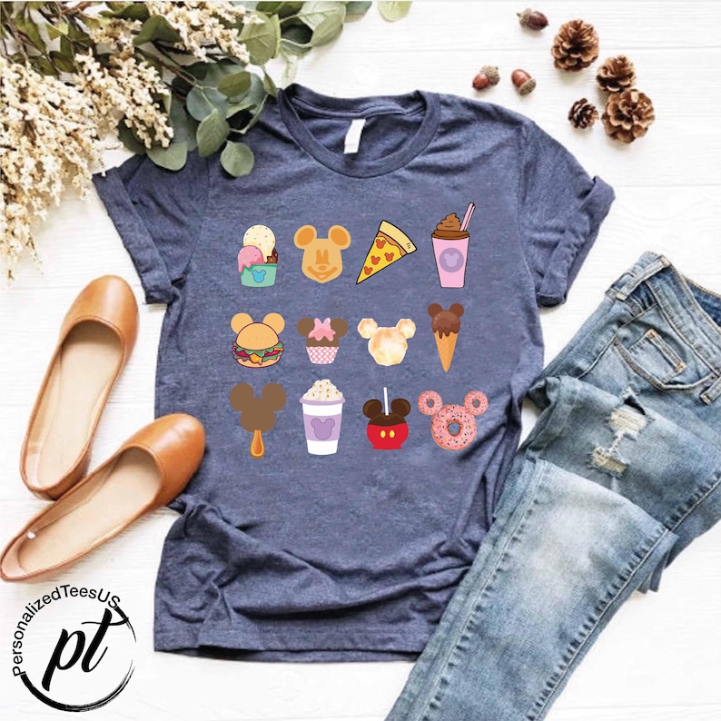 May include: A navy blue t-shirt with a variety of Disney-themed food and drink graphics, including Mickey Mouse ears, ice cream, popcorn, and a donut.