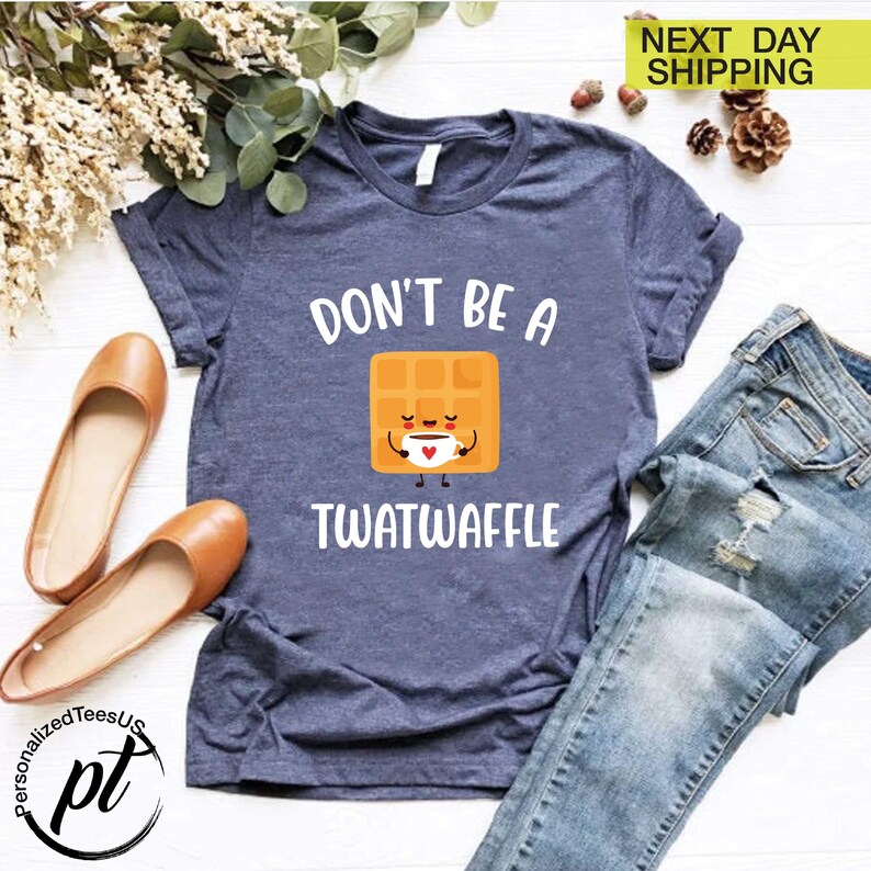 K&ouml;nnte beinhalten: Ein marineblaues T-Shirt mit dem Text "DON'T BE A TWATWAFFLE" und einer Cartoon-Waffel, die eine Kaffeetasse h&auml;lt. Das Shirt wird mit einer blauen Jeans und braunen Ballerinas kombiniert. Die Worte "NEXT DAY SHIPPING" stehen oben rechts.