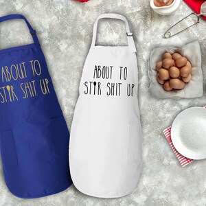 May include: Two kitchen aprons, one royal blue and one white, with the text "About to Stir Shit Up" printed on them.