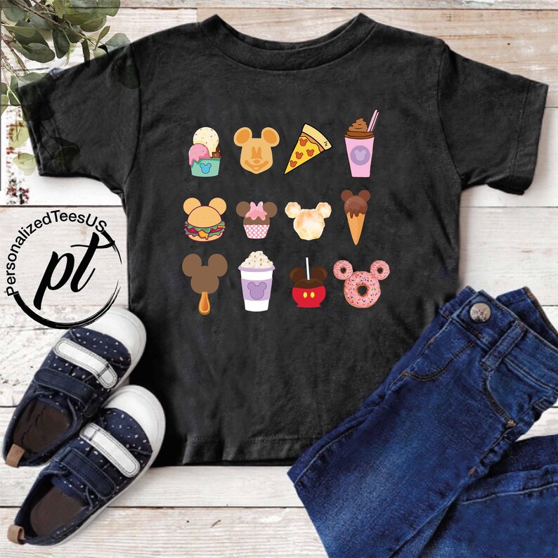 May include: Black t-shirt with a white and colorful graphic print of Mickey Mouse themed food items, including a Mickey Mouse ice cream cone, Mickey Mouse shaped hamburger, Mickey Mouse shaped donut, Mickey Mouse shaped pizza, Mickey Mouse shaped cupcake, Mickey Mouse shaped ice cream, Mickey Mouse shaped apple, and Mickey Mouse shaped popsicle.