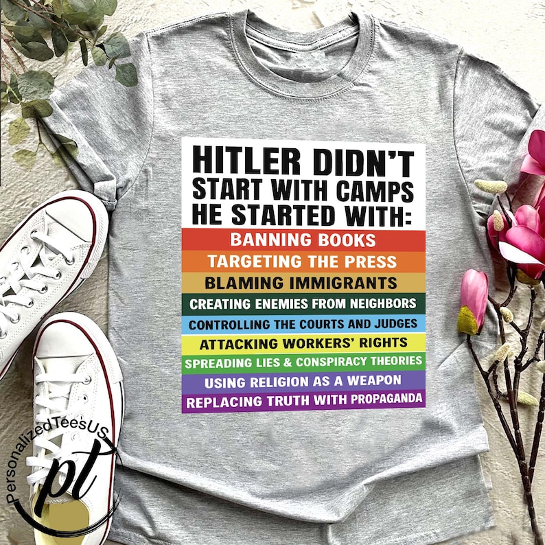 May include: A gray t-shirt with the text "HITLER DIDN'T START WITH CAMPS HE STARTED WITH:" followed by a list of actions in a rainbow-colored design. White canvas sneakers are visible on the left.