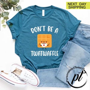 K&ouml;nnte beinhalten: T&uuml;rkisfarbenes T-Shirt mit dem Aufdruck "DON'T BE A TWATWAFFLE" und einer Cartoon-Waffel, die eine Kaffeetasse h&auml;lt. Das Shirt wird mit blauen Jeans und wei&szlig;en Turnschuhen kombiniert.