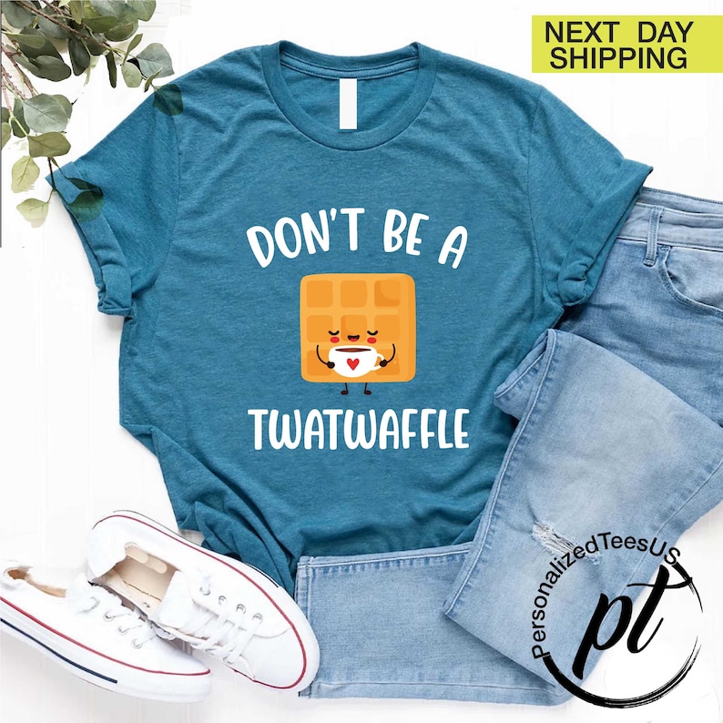 K&ouml;nnte beinhalten: T&uuml;rkisfarbenes T-Shirt mit dem Aufdruck "DON'T BE A TWATWAFFLE" und einer Cartoon-Waffel, die eine Kaffeetasse h&auml;lt. Das Shirt wird mit blauen Jeans und wei&szlig;en Turnschuhen kombiniert.