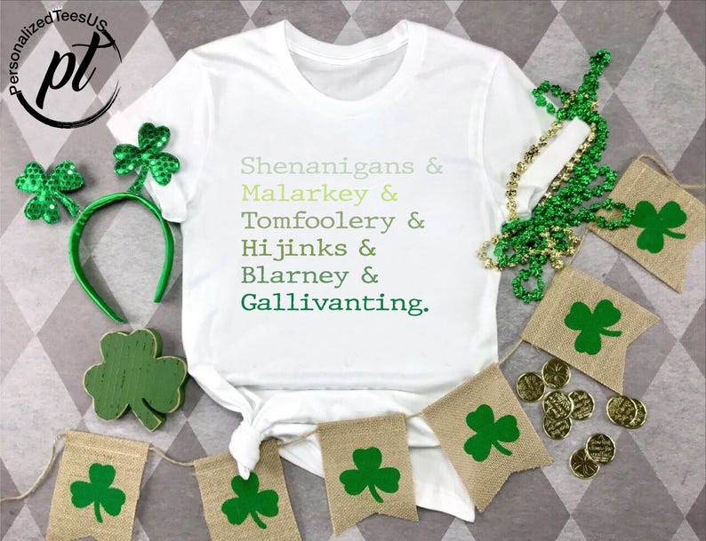 May include: White t-shirt with the text "Shenanigans & Malarkey & Tomfoolery & Hijinks & Blarney & Gallivanting." Green shamrock decorations, a headband, and gold coins are arranged around the shirt, celebrating St. Patrick's Day.