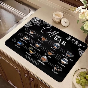 May include: A rectangular black coffee bar mat featuring white line art illustrations of various coffee drinks and their ingredients. The text reads Coffee Bar and Brewing Since 1997, with labels for Latte Macchiato, Cappuccino, Cold Brew, Romano, Black Eye, Espresso Freddo, Ra Coffee, Irish Coffee, Frappe, Espresso-Tonic, Iced Latte, and Affogato.