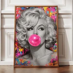 May include: A framed art print depicting Marilyn Monroe in black and white, blowing a pink bubblegum bubble. The background is a vibrant, multi-coloured abstract design with splashes of paint.