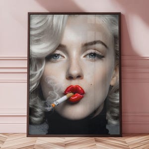 May include: A framed portrait of a woman with platinum blonde hair, blue eyes, and red lipstick, smoking a cigarette. The image is in a dark brown frame, with a black turtleneck. The background is a pink wall.