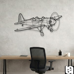 Op de afbeelding: Zwarte metalen vliegtuig wandkunst. Het vliegtuig is een dubbeldekker ontwerp met een grote propeller en gedetailleerde vleugels. Het kunstwerk is gemonteerd op een lichtgrijze muur boven een bureau en bureaustoel.