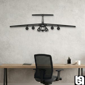 May include: Black metal airplane wall art. The artwork depicts a detailed outline of a large aircraft, including wings, engines, and tail. The piece is mounted on a textured, light-colored wall above a desk and chair.