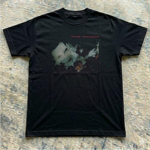Könnte beinhalten: Schwarzes T-Shirt mit dem Albumcover von The Cure's "Disintegration". Das Design zeigt ein Porträt in Grün- und Weißtönen, der Albumtitel ist rot gedruckt. Ein klassisches Band-T-Shirt.