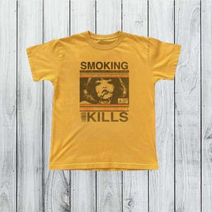 Op de afbeelding: Mosterdgeel T-shirt met een bruine afbeelding met de tekst "SMOKING KILLS". De afbeelding bevat een sepia-afbeelding van een rokende persoon. Het shirt is gemaakt van een zacht materiaal en heeft korte mouwen.