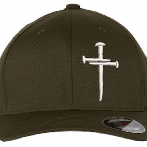 May include: Olive green baseball cap featuring a white embroidered cross made of nails. The cap has a curved brim and a small button on top. The Flexfit brand label is visible on the brim.