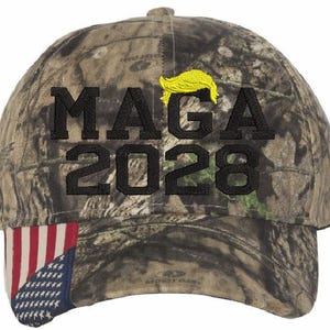 May include: Camouflage baseball cap with a black embroidered 'MAGA 2028' and a yellow hairpiece. The cap has a red, white and blue American flag on the underside of the brim.
