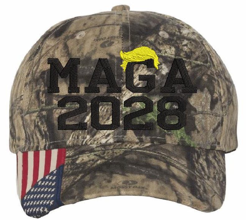 May include: Camouflage baseball cap with a black embroidered 'MAGA 2028' and a yellow hairpiece. The cap has a red, white and blue American flag on the underside of the brim.