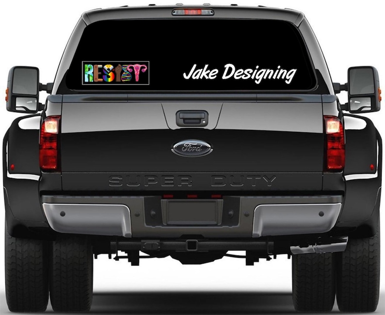 May include: Rear view of a black Ford Super Duty truck with a window decal. The decal on the top left says "RESET" in rainbow colors. The decal on the top right says "Jake Designing" in white script.
