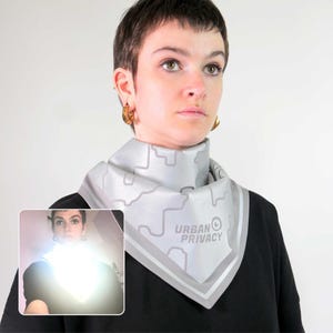 May include: A light gray square scarf with a geometric design and the text "URBAN PRIVACY" in gray. The scarf has a light gray border and is worn around the neck.
