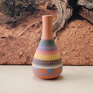 May include: A terracotta-colored vase with a narrow neck and a rounded body. The vase is adorned with horizontal bands of color, including blue, yellow, pink, and gray. The design is reminiscent of Native American pottery.