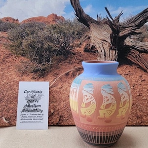 May include: A hand-painted Native American pottery vase with a light blue rim and base, featuring Kokopelli figures in yellow and blue on a peach background. Includes a certificate of authenticity.