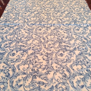 K&ouml;nnte beinhalten: Wei&szlig;er Stoff mit einem blauen und wei&szlig;en Blumenmuster. Das Muster zeigt komplizierte Wirbel und Bl&auml;tter.